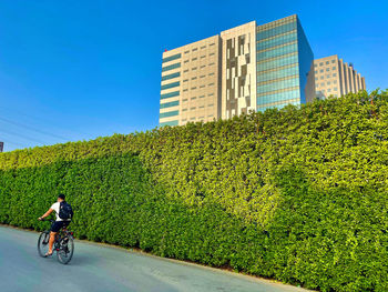 Man riding bicycle by building in city against sky