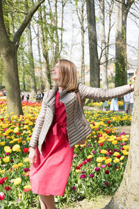 Happy young woman stands among the flower beds in the park and smiles with enjoy