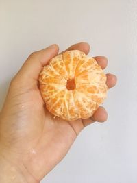 Close-up of hand holding orange slice over white background