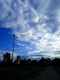 Street by silhouette trees against blue sky