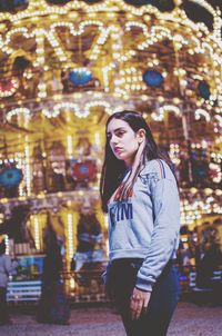 Young woman standing against illuminated amusement park ride