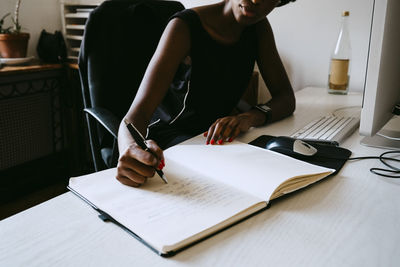 Female entrepreneur writing in diary on desk at office