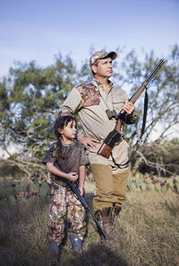 Hunters holding rifle and looking away while standing on grassy field