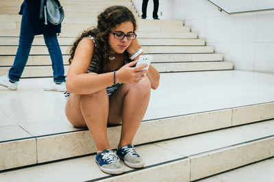 Teenage girl using smart phone while sitting on staircase