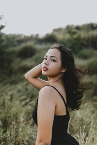 Portrait of young woman looking away while standing on field