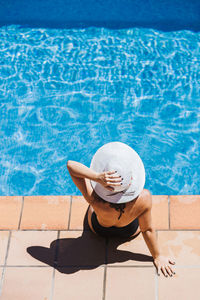 Young woman wearing hat sitting at poolside on sunny day
