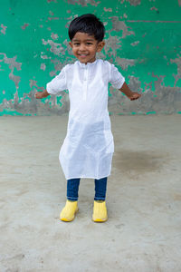 A smiling kid is posing for a photo wearing white punjabi and blue jeans.