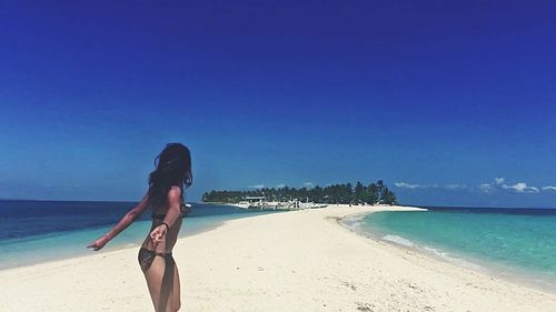 Rear view of woman standing on beach against clear sky