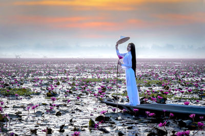 Woman standing by sea against sky during sunset