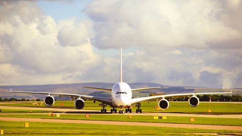 Airplane flying over grassy landscape against cloudy sky