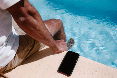 Businessman sitting poolside with mobile phone