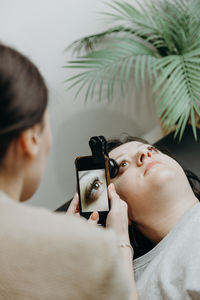 A girl cosmetologist takes pictures of a client s eyelashes on a smartphone.