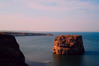 Rock formation in sea against sky during sunset