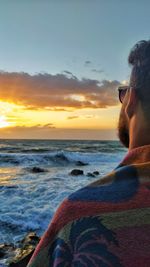 Side view of man looking at sea against sky during sunset
