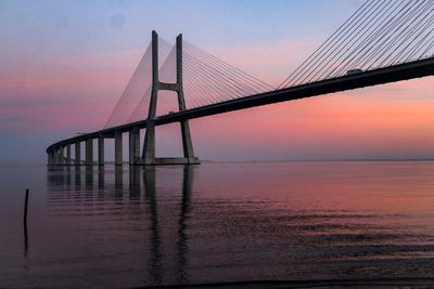 Suspension bridge over sea against sky during sunset