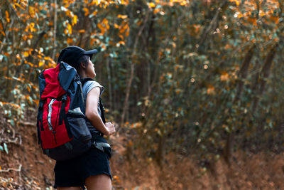 Woman with backpack standing against trees in forest