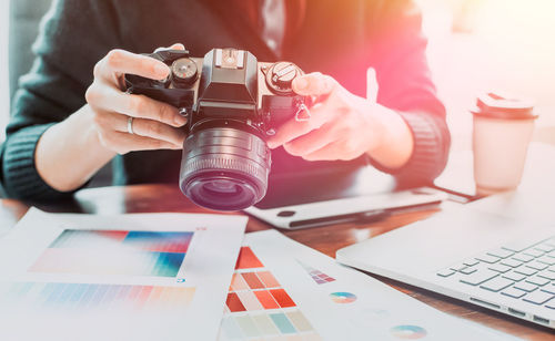 Midsection of design professional holding digital camera at desk in office