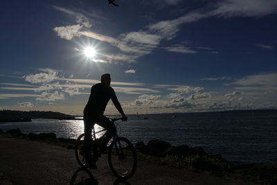 Man sitting on bicycle by sea against sky during sunset