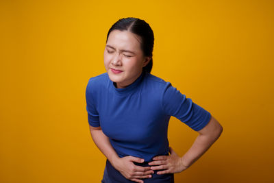 Young woman standing against yellow background