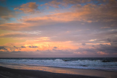 Scenic view of beach against cloudy sky during sunset