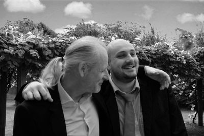 Smiling friends with arm around standing against plants