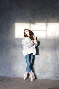 Full length portrait of woman standing against wall