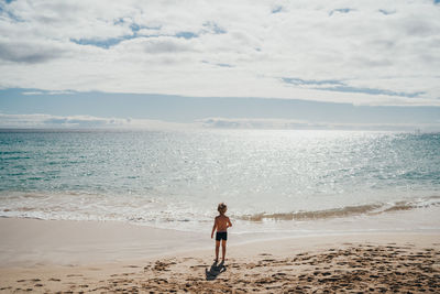 Boy walking into the water at the beach on a sunny day on vacation