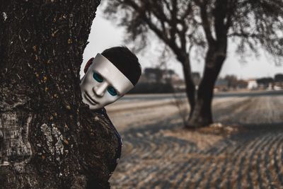 Man wearing mask hiding behind tree on field