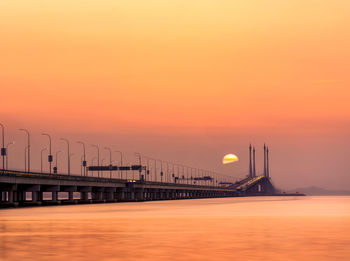 Bridge over sea against orange sky