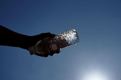 Low angle view of hand holding umbrella against clear blue sky