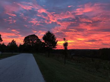 Road by trees against sky during sunset