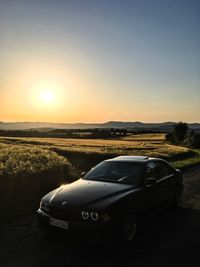 Car on landscape against sky during sunset