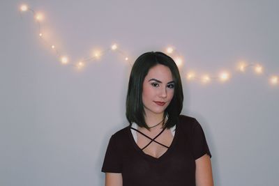 Portrait of young woman standing against illuminated lamp