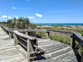 Wooden railing by sea against sky