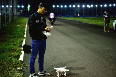 Full length of man with drone standing on road at night