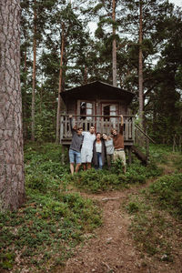 Cheerful friends with arms around standing against house in forest during vacation