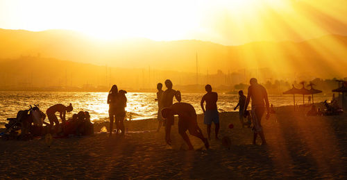 Silhouette people at beach against sky during sunset