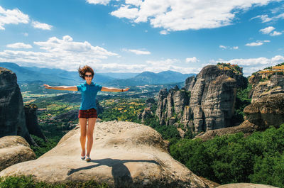 Portrait of happy woman with arms outstretched standing on rock against landscape