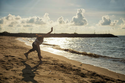 Full length of woman exercising on beach against sky