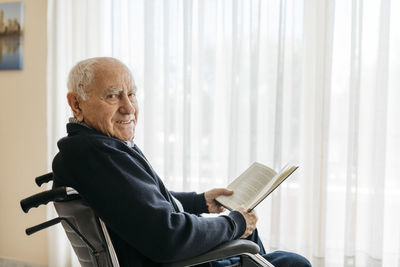 Portrait of smiling senior man sitting in wheelchair with a book