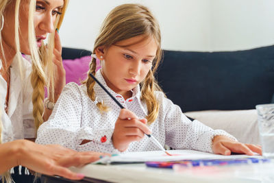 Teacher assisting girl in painting at classroom