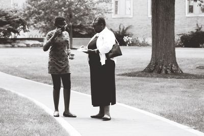 Female friends talking while standing on footpath at park