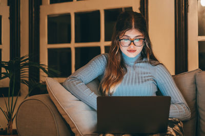 Young woman using laptop while sitting on sofa at home