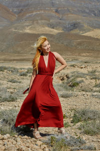 A blonde woman in a red dress in the desert on a windy day person