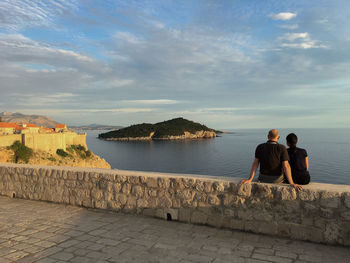 Rear view of man and woman looking at view of sea against sky