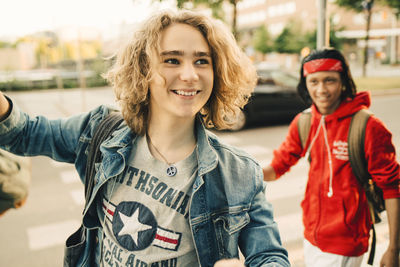 Smiling young man looking away while friend standing in background on street