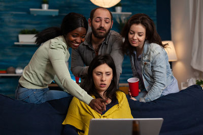 Portrait of smiling friends using digital tablet while sitting on sofa at home