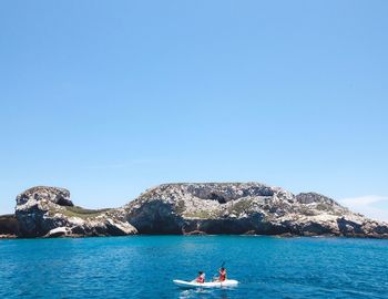 People kayaking in sea against clear blue sky