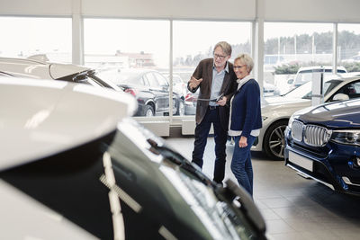 Senior couple discussing over car in showroom