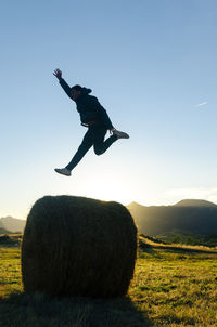 Man jumping on top of hay bale in sunlight